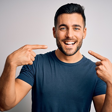 Man in blue shirt smiling and pointing to his teeth