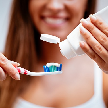 Woman squeezing toothpaste onto red and white toothbrush